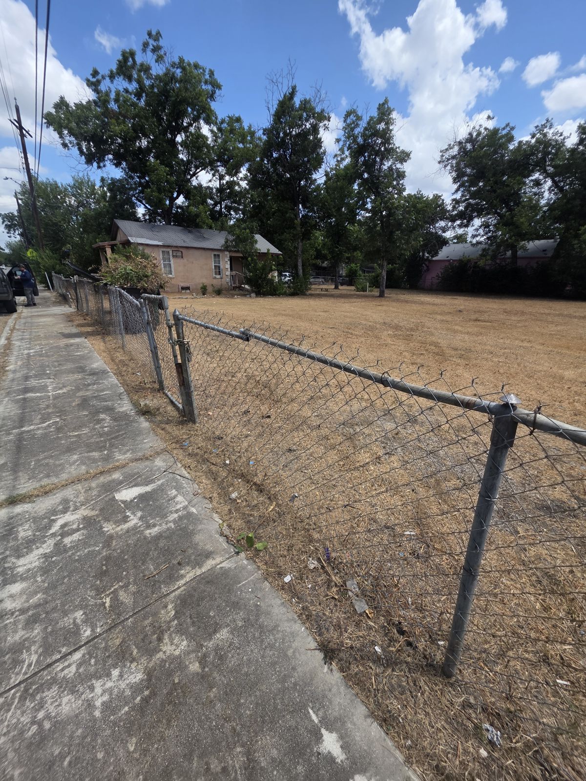 Chain-link fence corner with cleared grass beside the sidewalk
